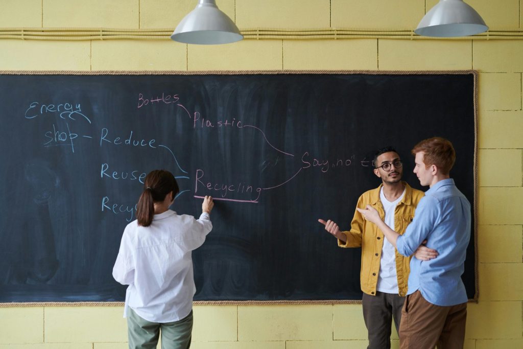Three people engaging in a discussion about recycling at a blackboard.